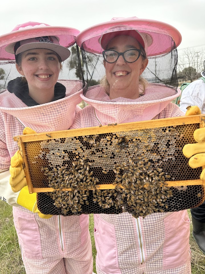 A picture of two women in bee suits holding a bee frame at a beekeeping class